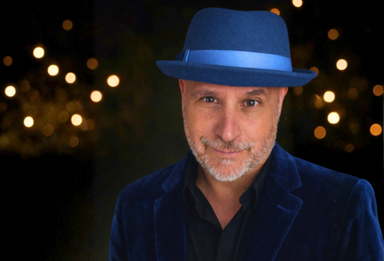 John Moyer, comedy hypnotist, in a blue hat and velvet jacket under stage lights